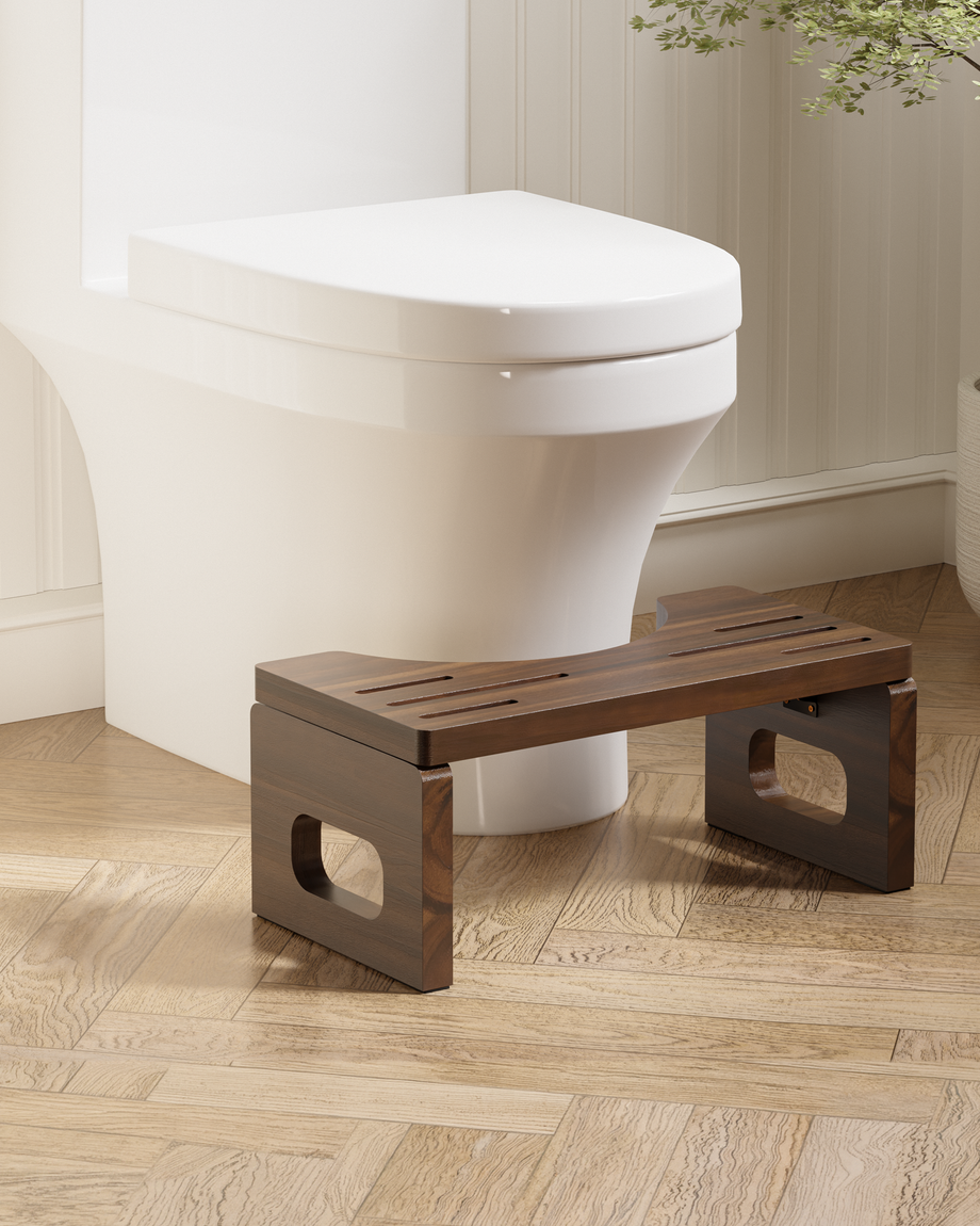 A dark brown wooden toilet step stool placed in front of a white toilet on a light wood herringbone floor.