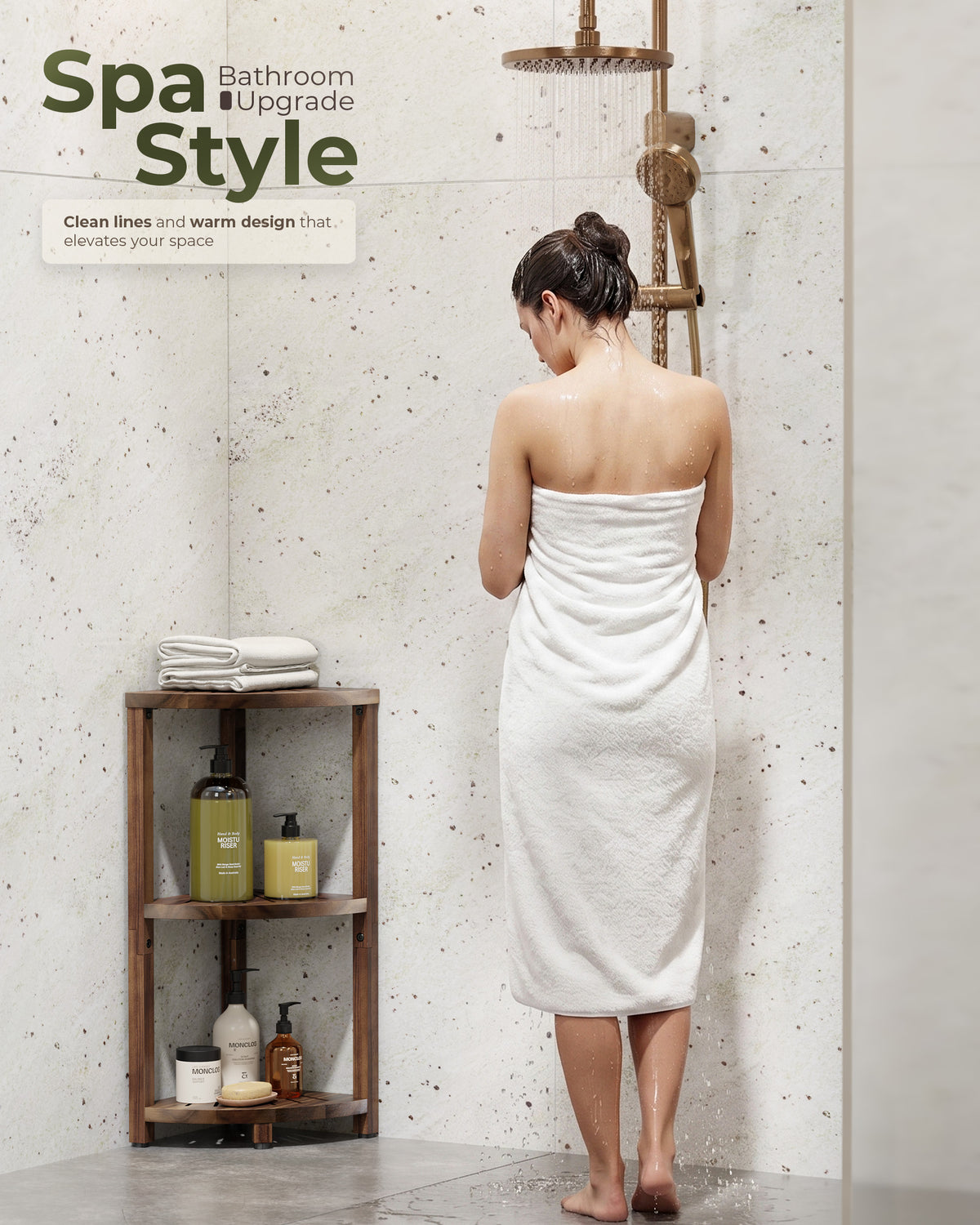 A woman wrapped in a white towel stands in a bathroom shower corner with a warm brass shower fixture. A small wooden shelf with toiletries sits to the left.