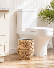 White toilet in a bathroom with a woven trash can and a plant.