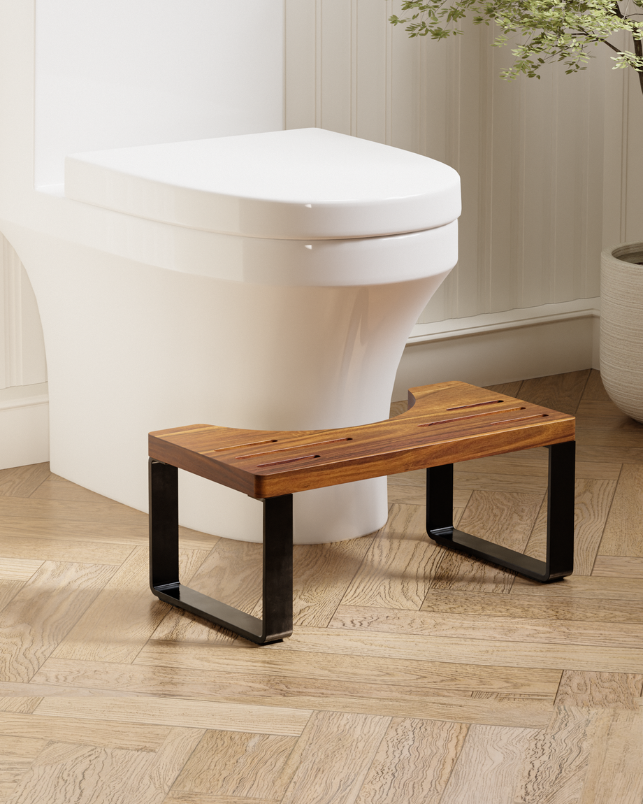A wooden toilet step stool with black metal legs, positioned in front of a white toilet on a light wood herringbone floor.