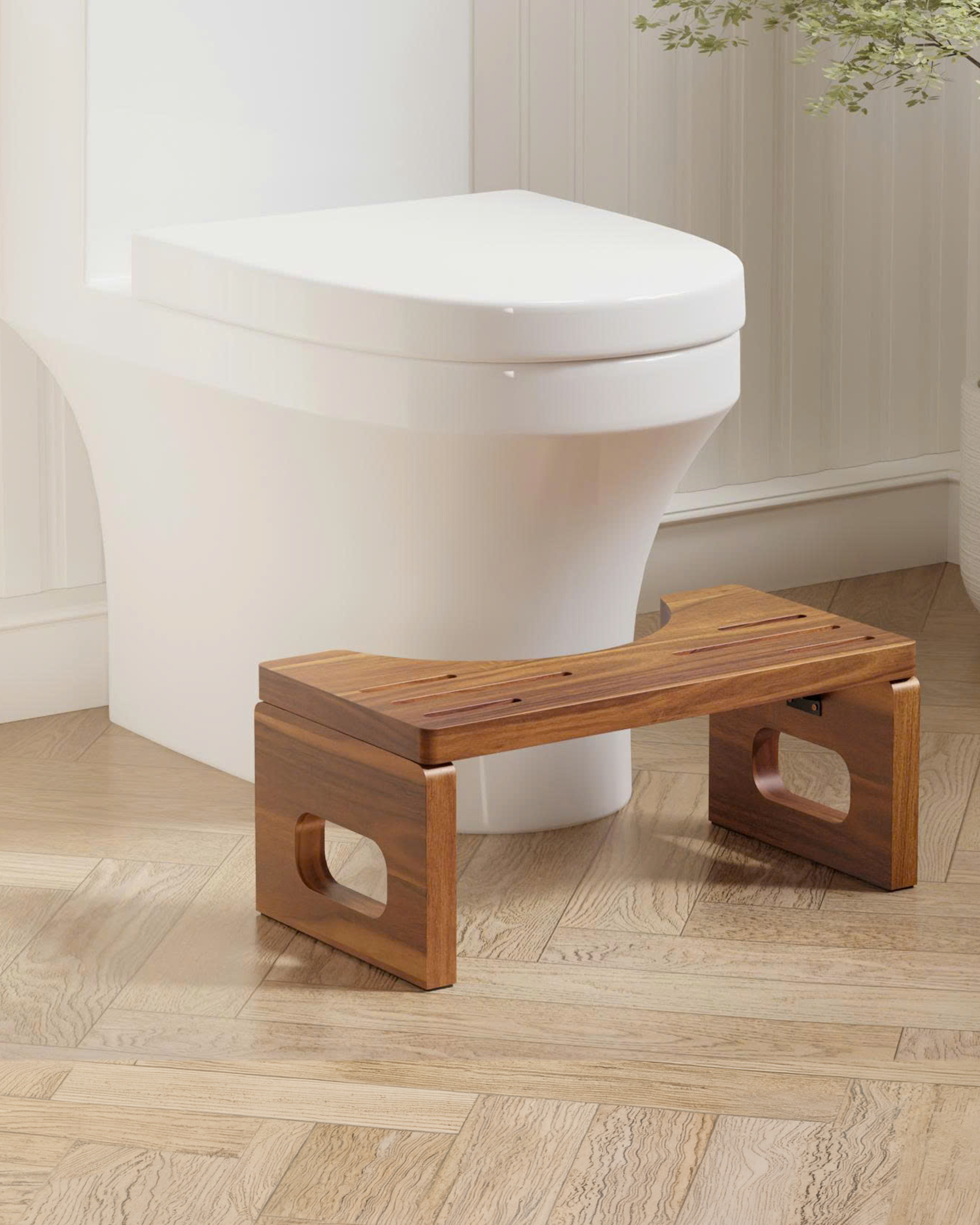 A wooden bathroom step stool with cutout legs, positioned in front of a white toilet on a light wood herringbone floor.