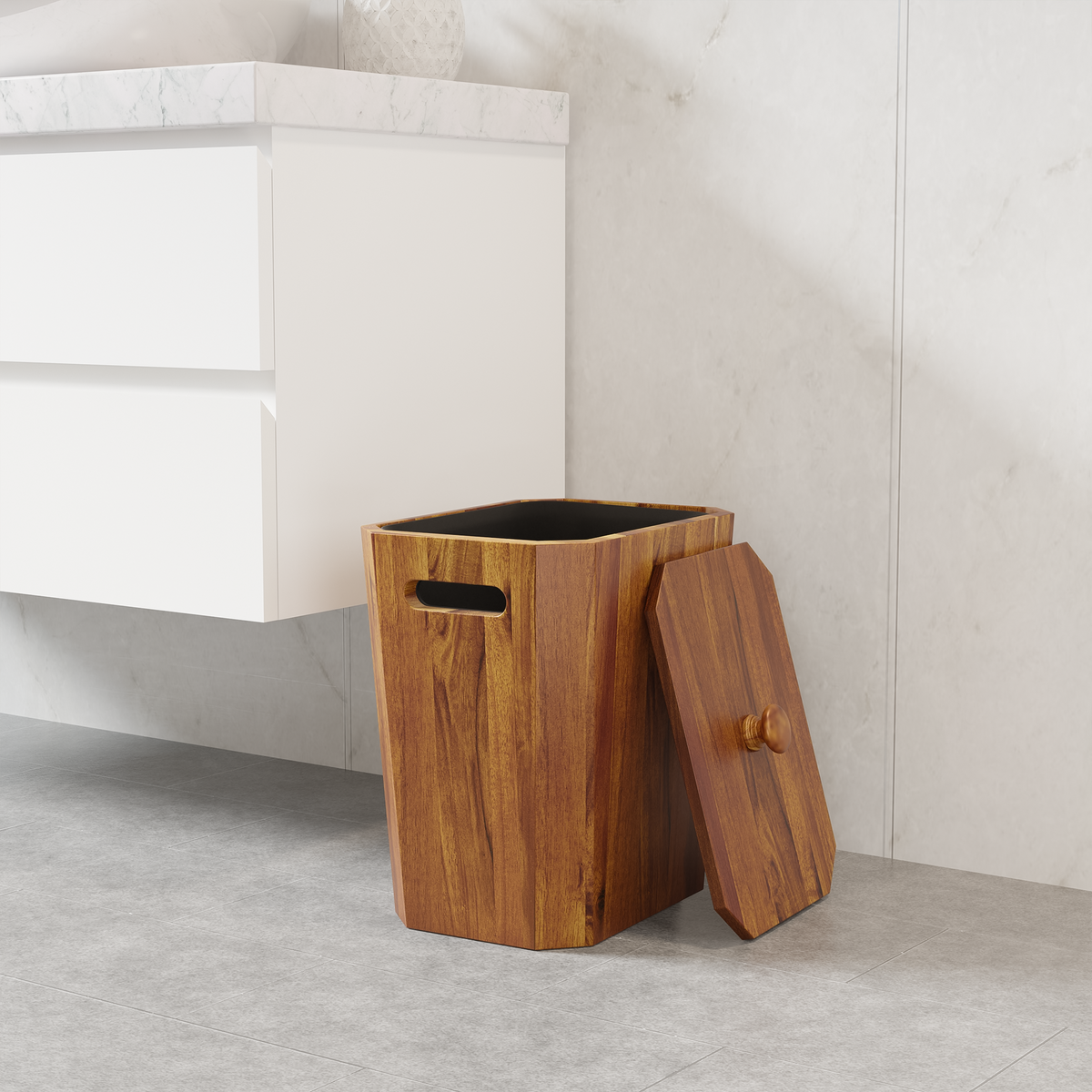 A rectangular wooden wastebasket with a hinged lid leaning against it, placed beside a white bathroom vanity on a light gray tiled floor.